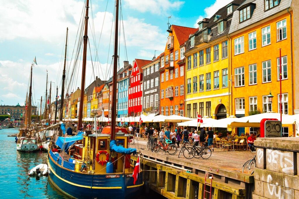 A photo of Copenhagen, Denmark. Colourful houses are seen by the river, with small boats docked. 